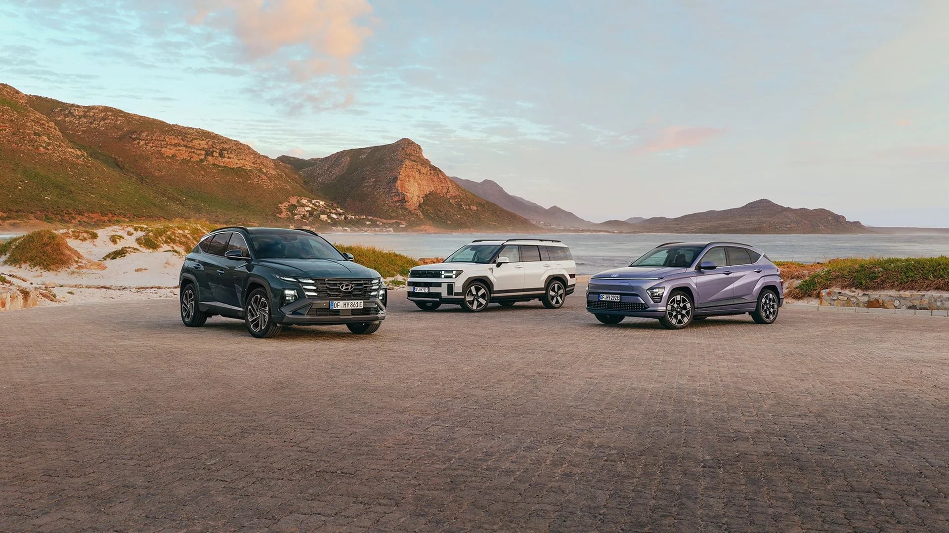 Hyundai TUCSON, SANTA FE och KONA uppställda vid en kustväg i kvällsljus
